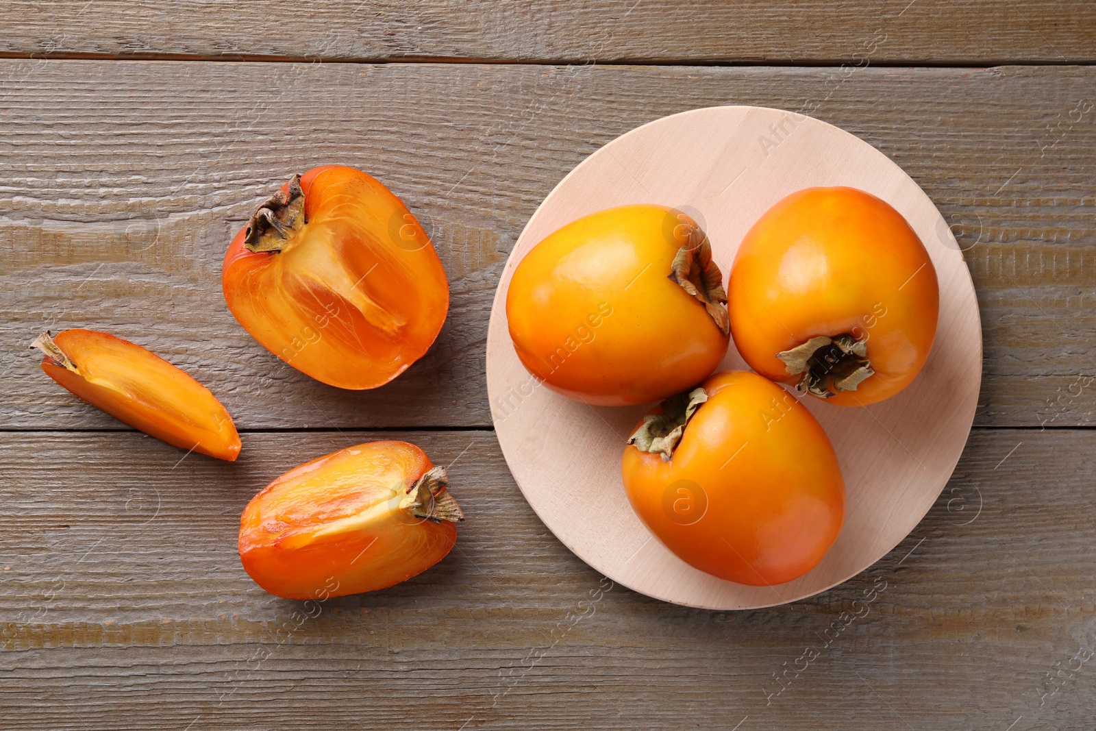 Photo of Whole and cut delicious ripe persimmons on wooden table, flat lay