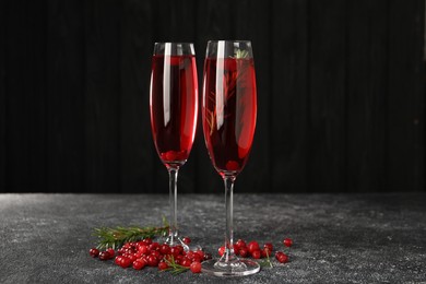 Tasty cranberry cocktail with rosemary in glasses on gray textured table against dark background