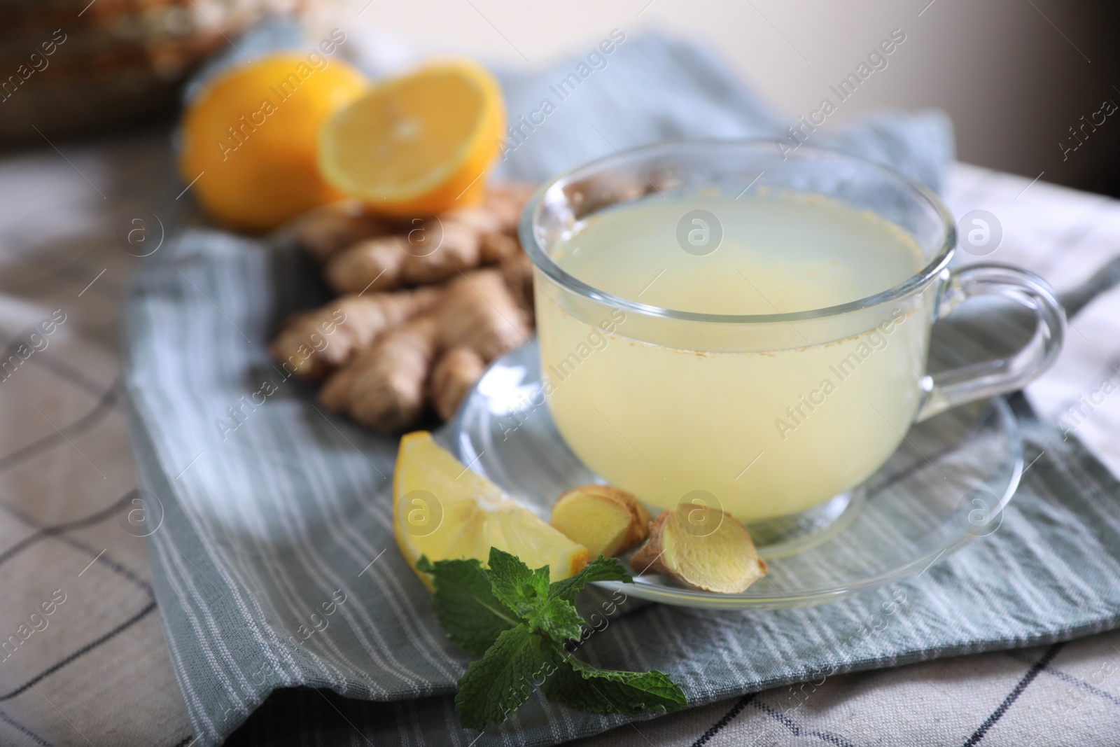Photo of Glass of aromatic ginger tea and ingredients on white checkered tablecloth, closeup. Space for text