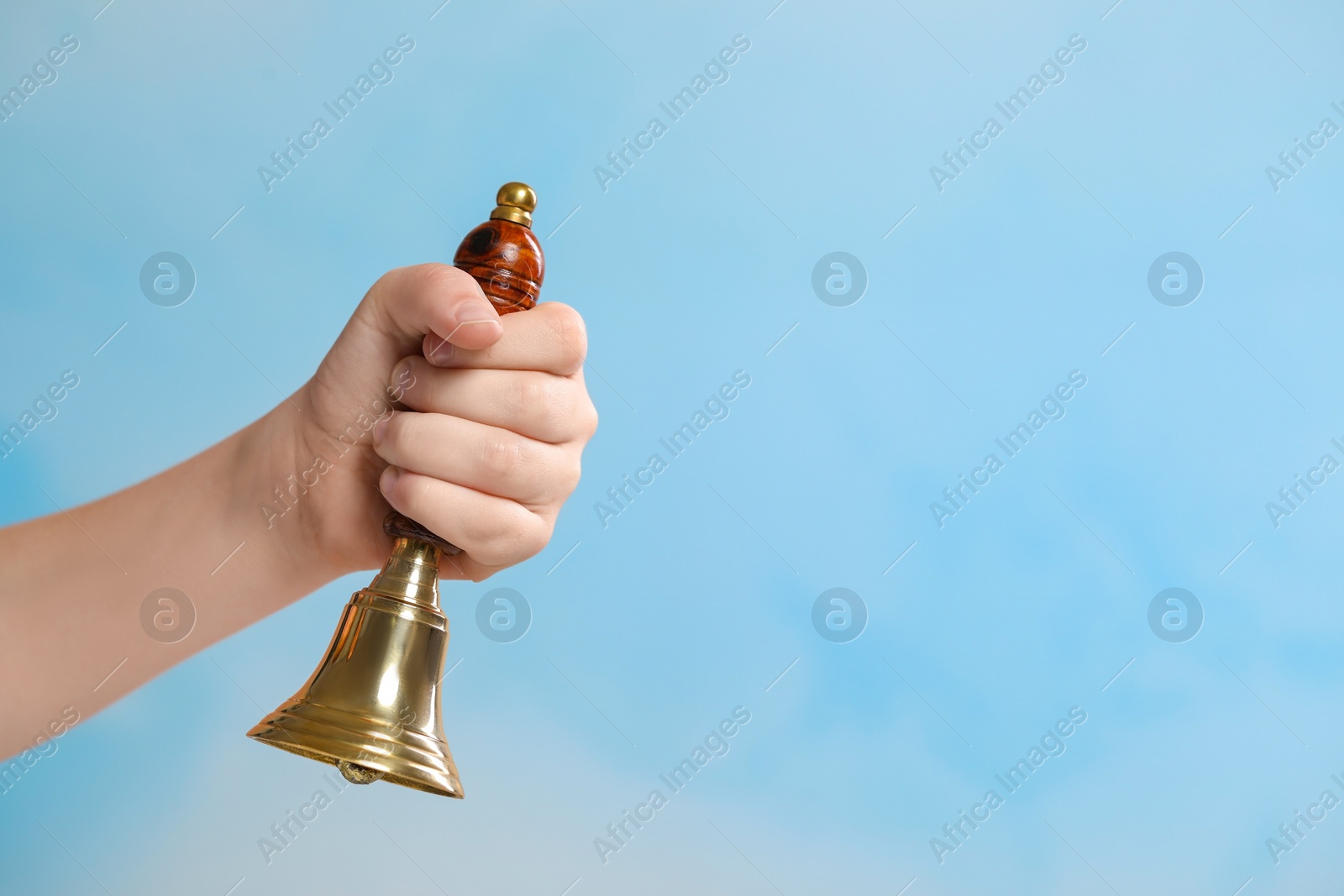 Photo of Pupil with school bell on light blue background, closeup. Space for text