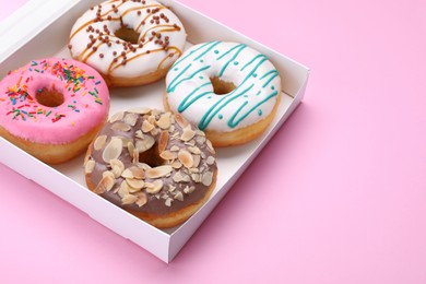 Photo of Box with different tasty glazed donuts on pink background. Space for text