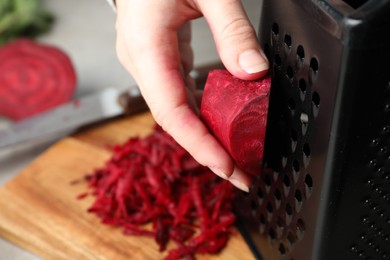 Photo of Woman grating fresh red beet at table, closeup