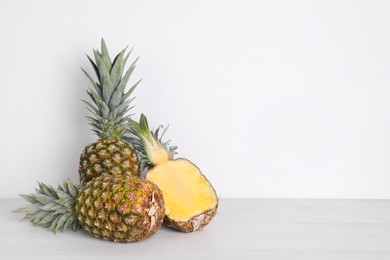 Photo of Whole and cut ripe pineapples on white wooden table. Space for text