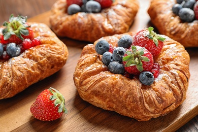 Photo of Fresh delicious puff pastry with sweet berries on wooden board, closeup