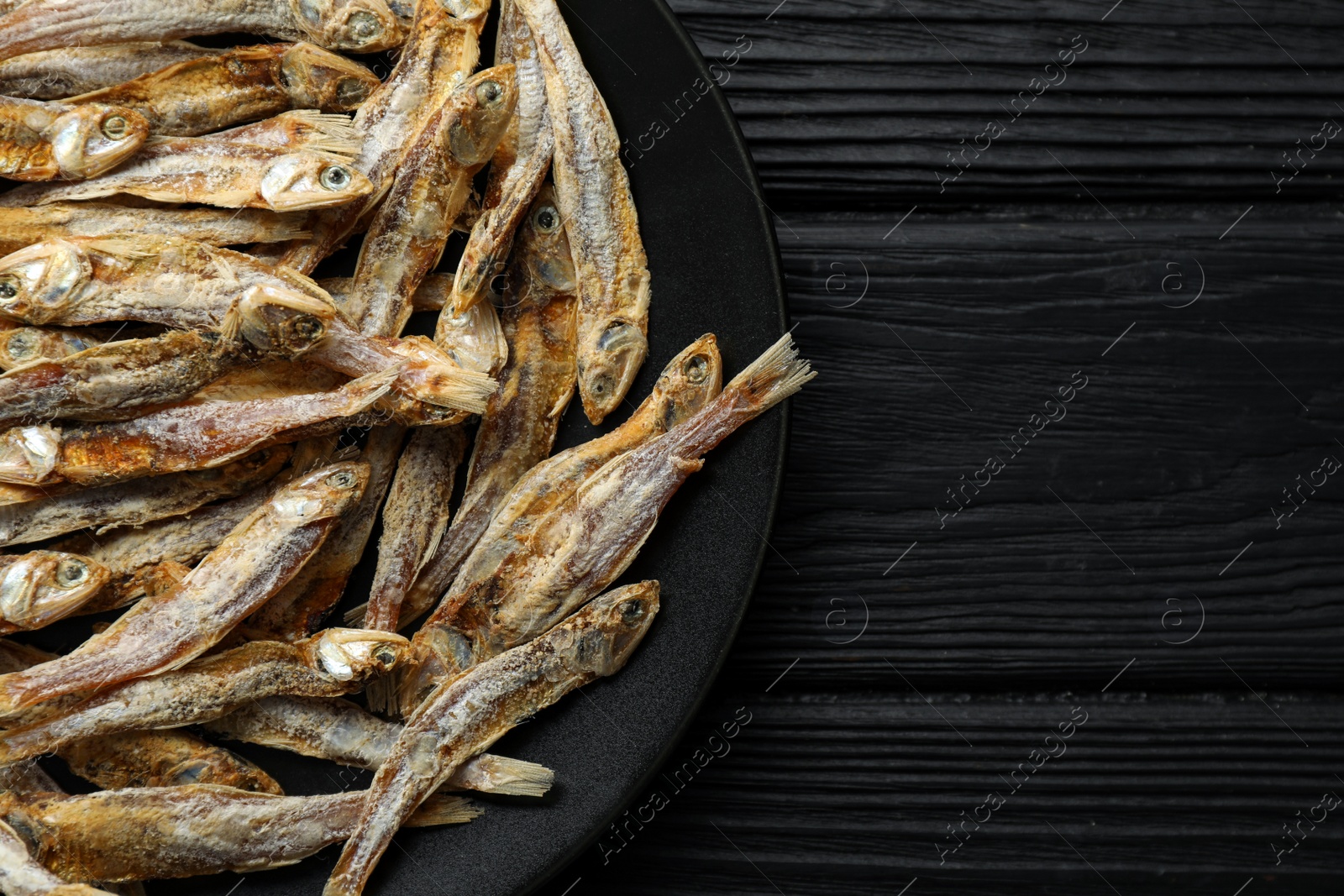 Photo of Delicious dried anchovies on black wooden table, top view. Space for text