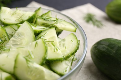 Photo of Cut cucumber with dill in glass bowl and fresh vegetable on table, closeup