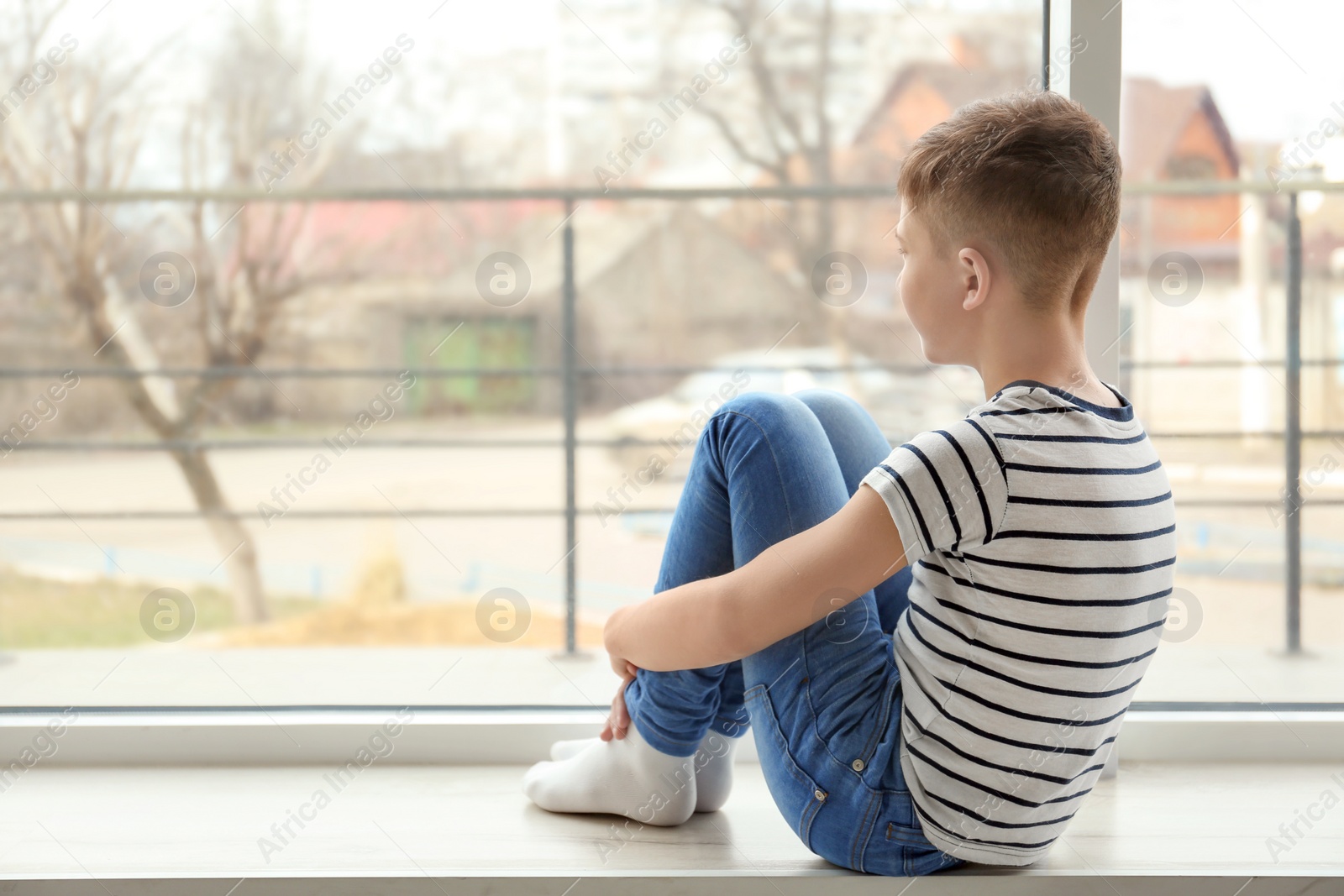 Photo of Lonely little boy sitting on windowsill. Autism concept