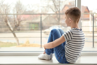 Lonely little boy sitting on windowsill. Autism concept