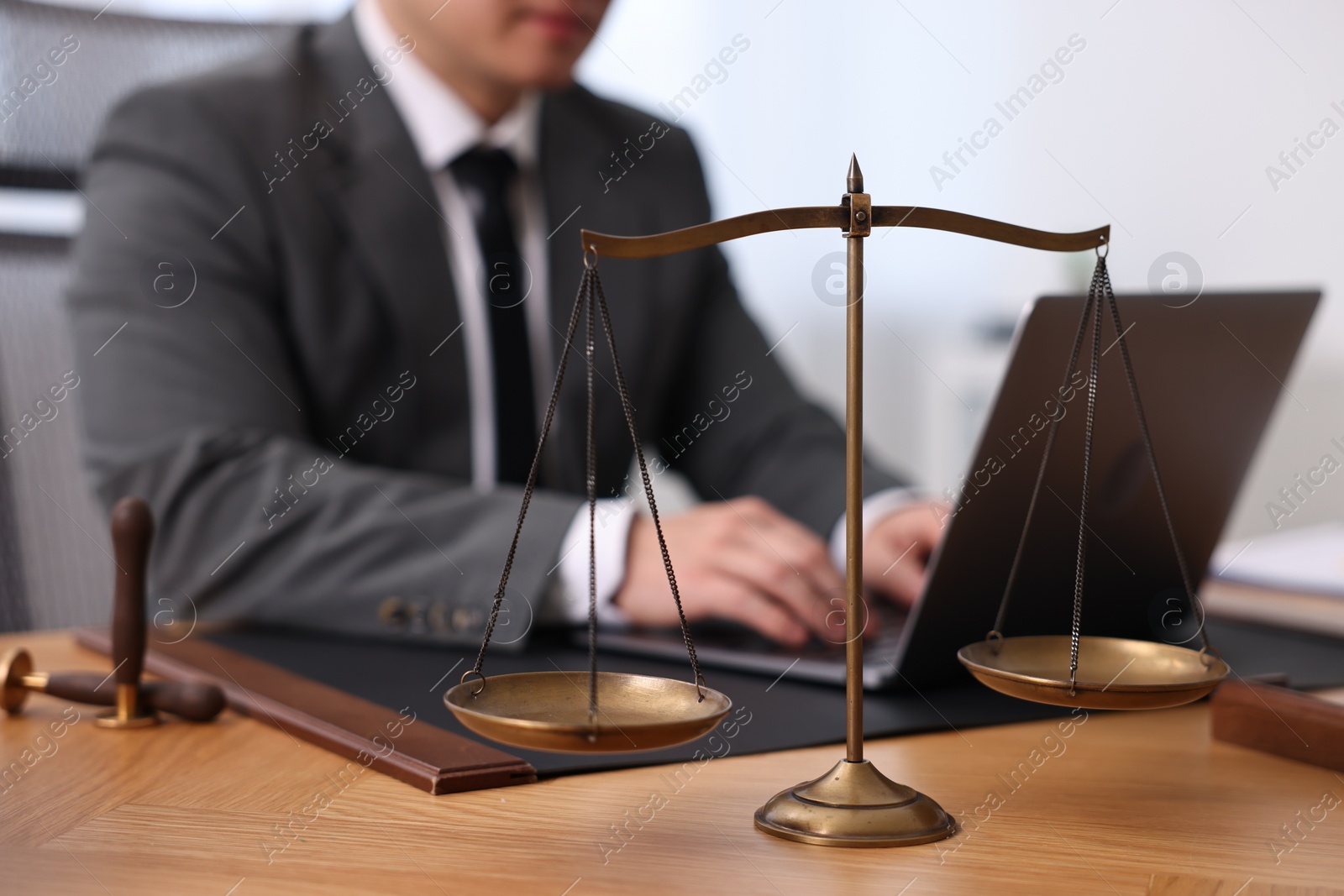 Photo of Notary working with laptop at wooden table in office, focus on scales of justice