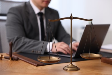 Photo of Notary working with laptop at wooden table in office, focus on scales of justice