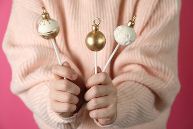 Woman holding delicious Christmas themed cake pops on pink background, closeup