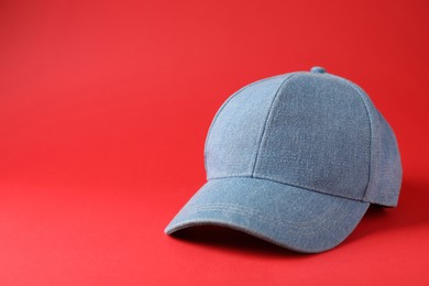 Photo of Stylish light blue denim baseball cap on red background. Space for text