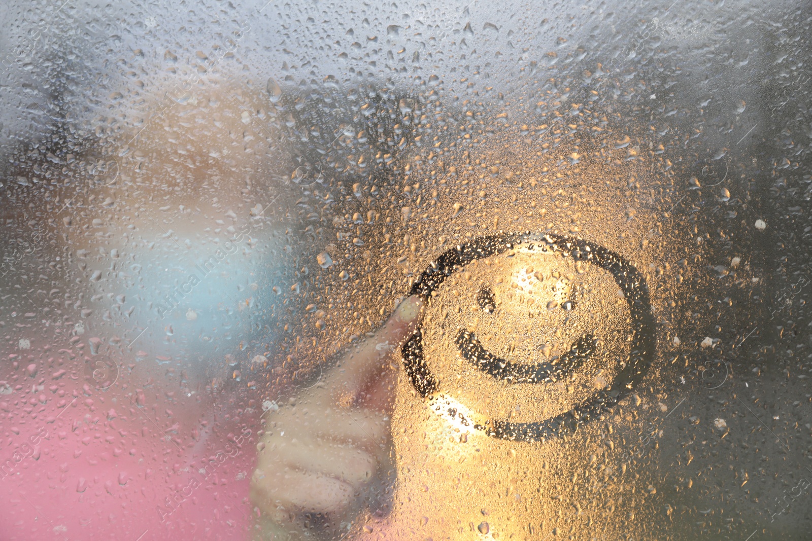 Photo of Woman drawing happy face on foggy window at rainy weather, closeup