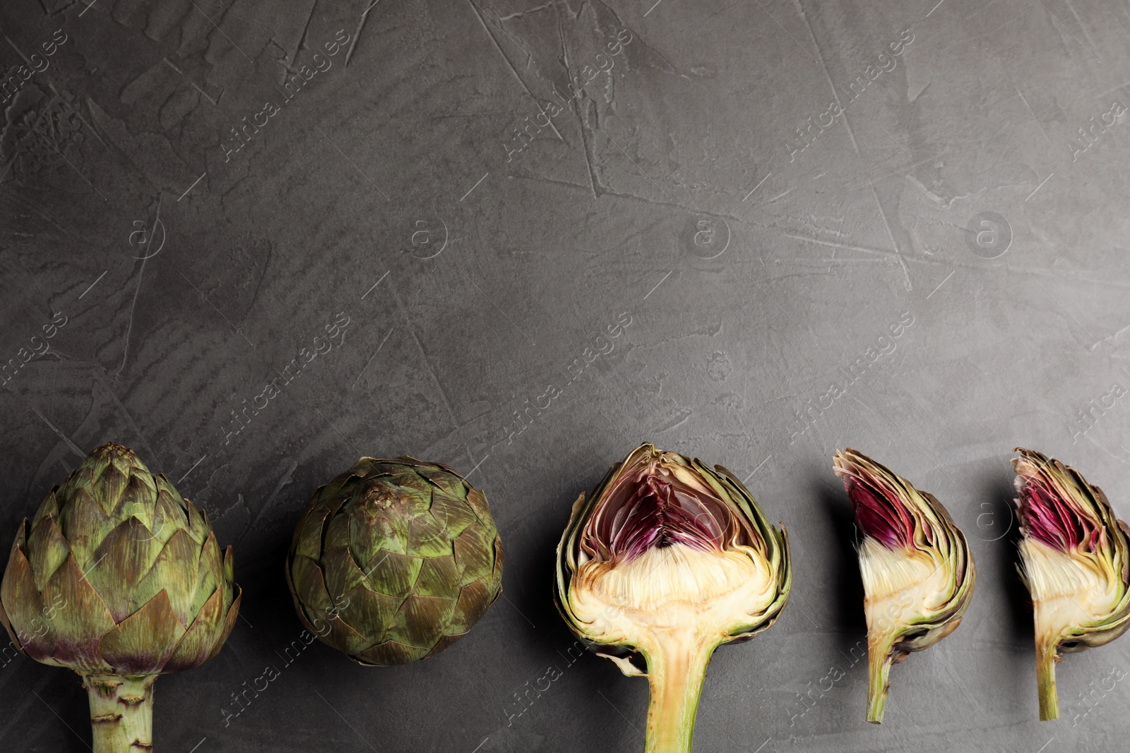 Photo of Cut and whole fresh raw artichokes on grey table, flat lay. Space for text