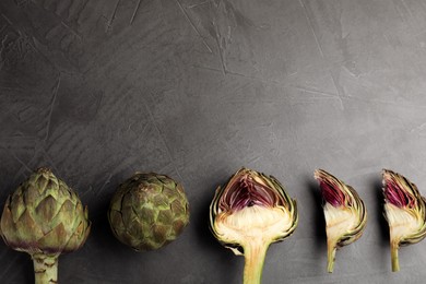 Cut and whole fresh raw artichokes on grey table, flat lay. Space for text