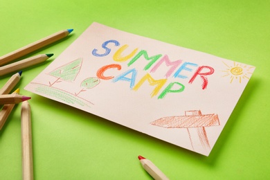 Paper with written text SUMMER CAMP, drawings and different pencils on color background, closeup