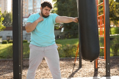 Photo of Young overweight man kicking heavy bag on sports ground