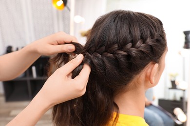 Photo of Professional stylist braiding client's hair in salon