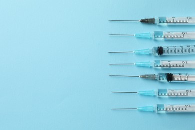 Disposable syringes with needles and medicine on light blue background, flat lay. Space for text