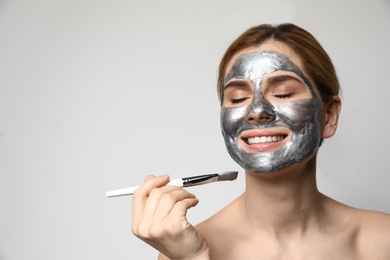 Photo of Beautiful woman applying mask onto face against light background. Space for text