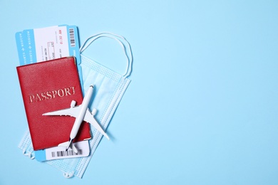 Flat lay composition with passport, protective mask and toy plane on light blue background. Space for text