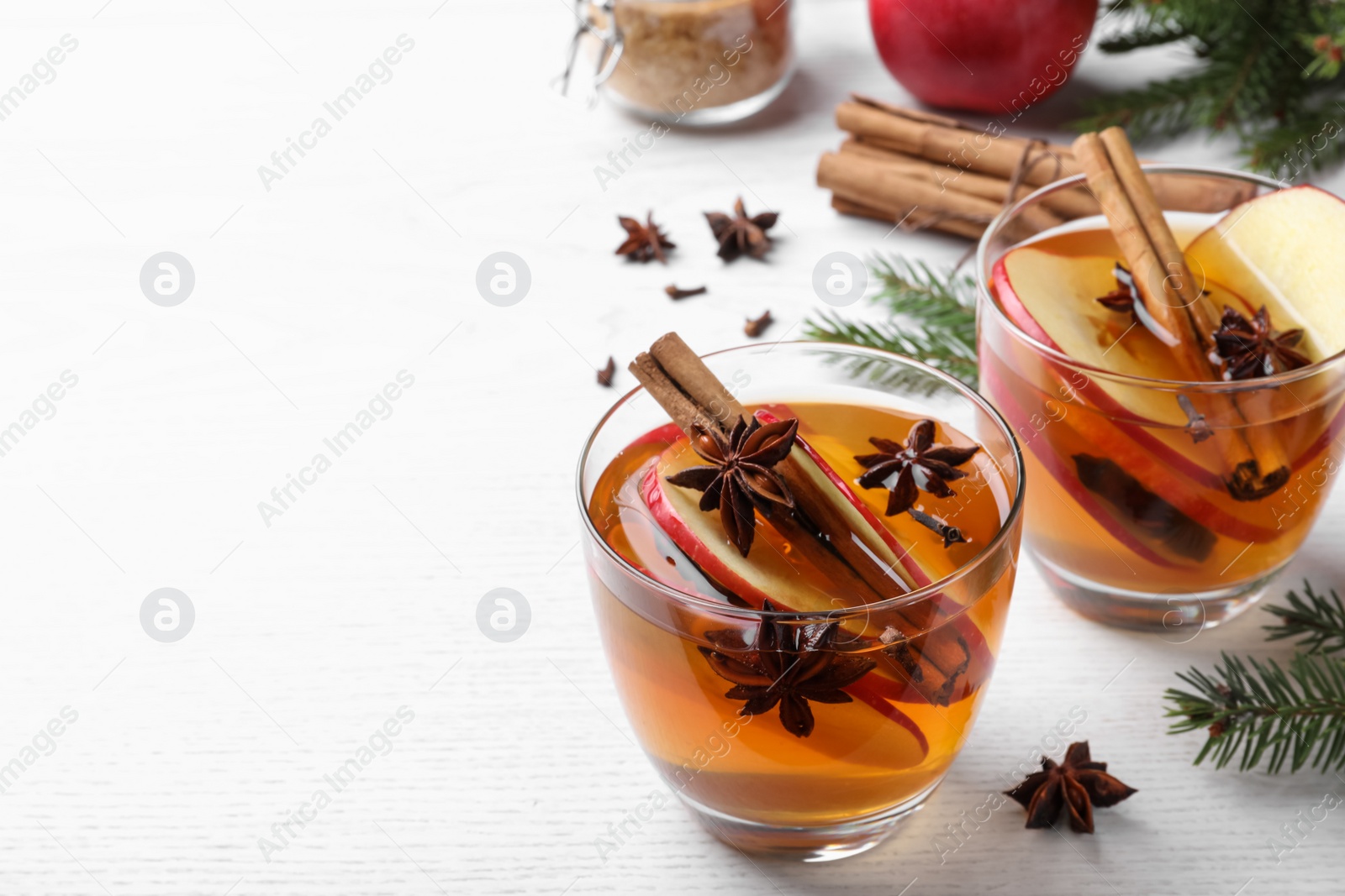 Photo of Hot mulled cider and fir branches on white wooden table, space for text