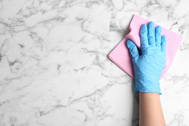 Photo of Woman in gloves wiping white marble table with rag, top view. Space for text