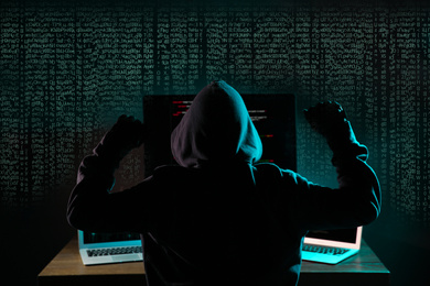 Hacker near computers in dark room and digital symbols on background. Cyber crime concept