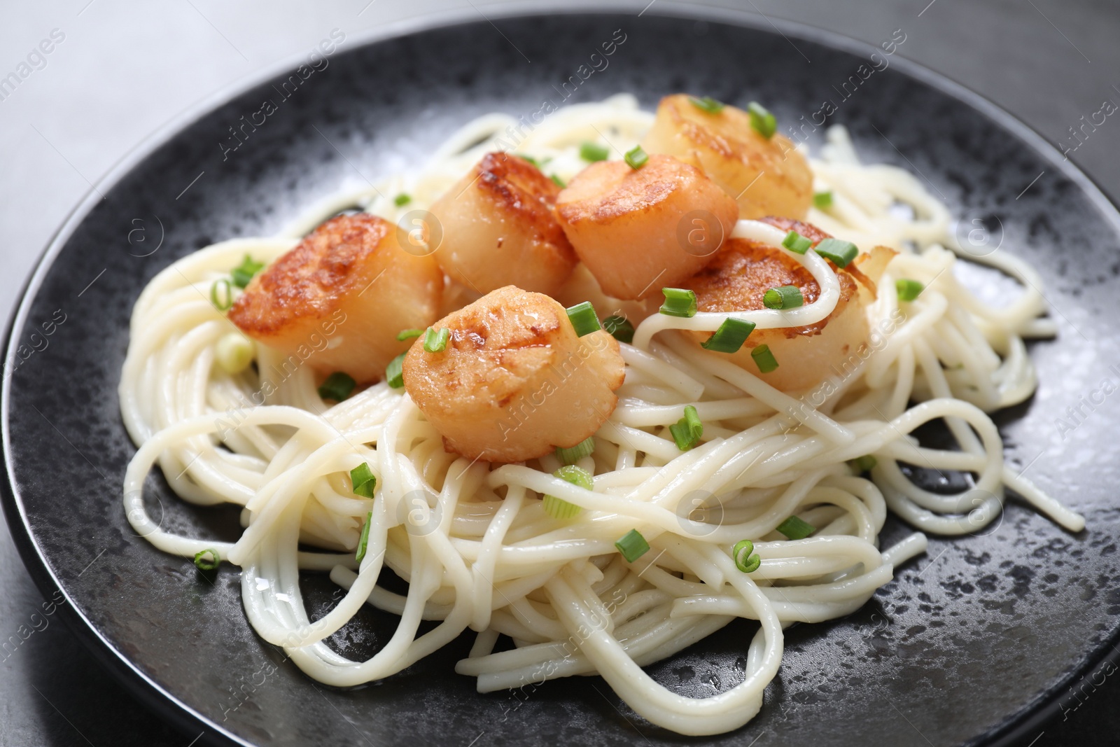 Photo of Delicious scallop pasta with green onion on grey table, closeup