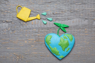 Photo of Happy Earth Day. Flat lay composition with plasticine planet and watering can on grey wooden table