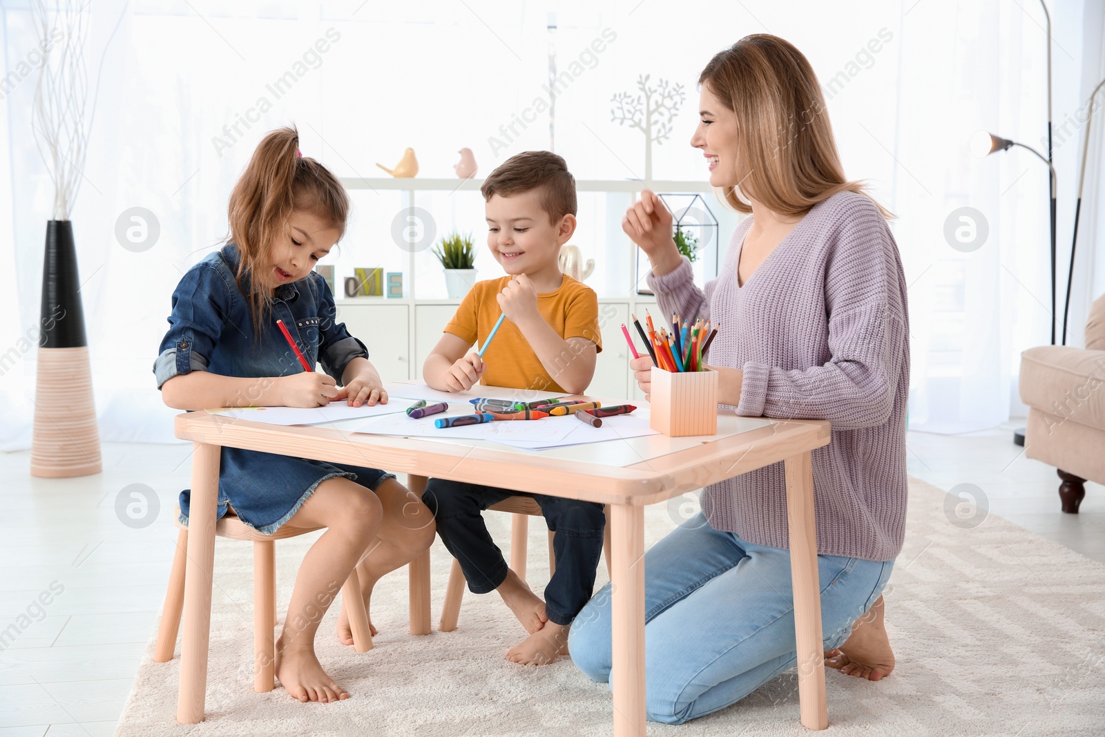 Photo of Cute little children and their nanny drawing at home