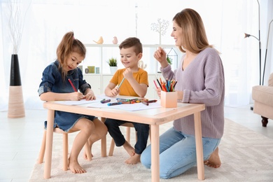 Photo of Cute little children and their nanny drawing at home