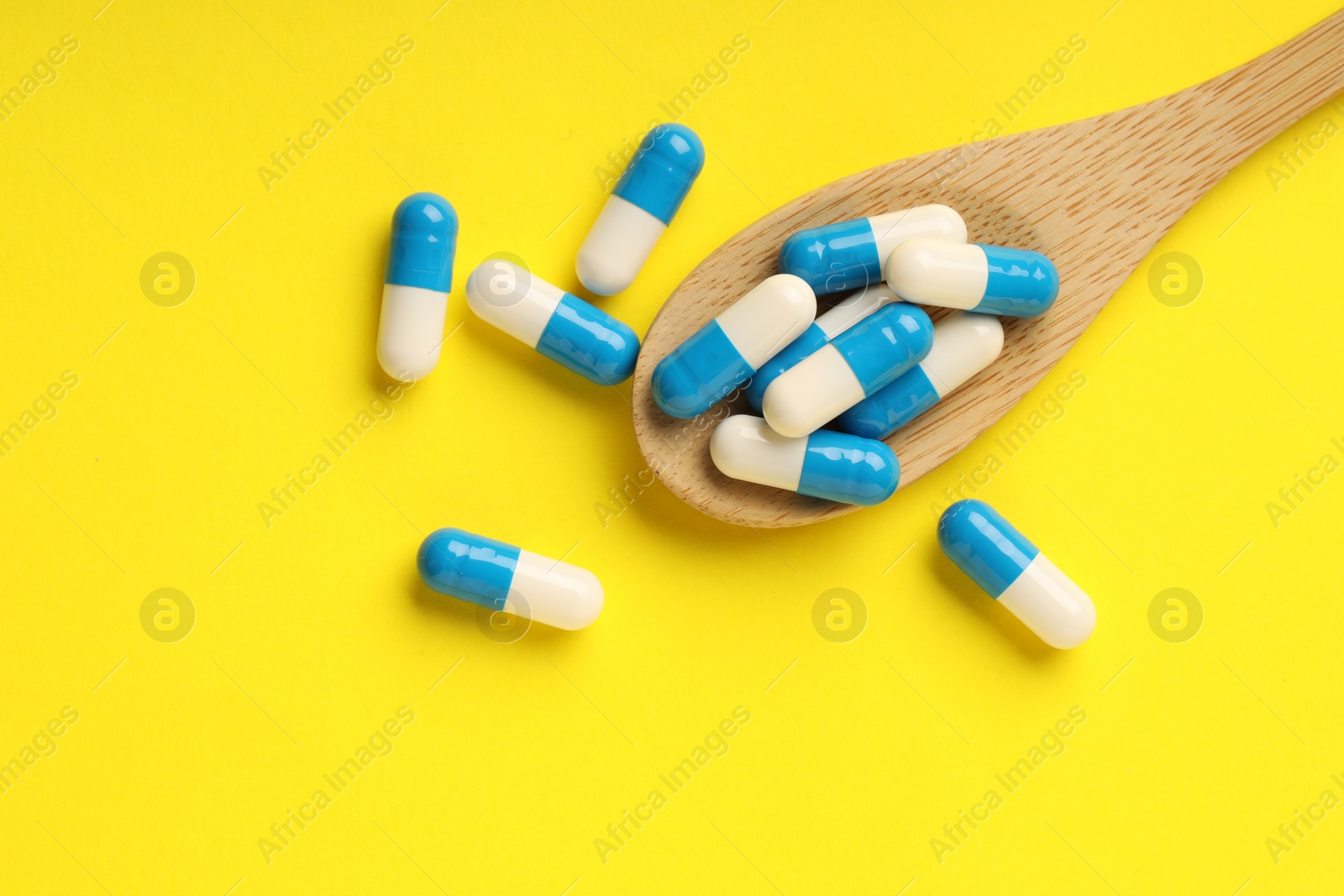 Photo of Antibiotic pills and spoon on yellow background, top view