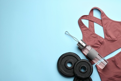 Sportswear, weight plates and water bottle on light blue background, flat lay with space for text. Gym workout