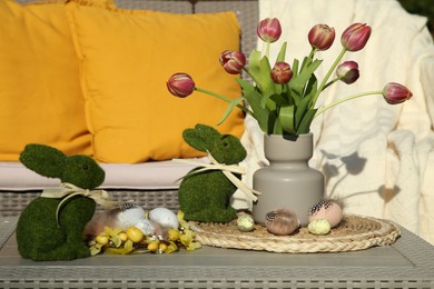 Photo of Terrace with Easter decorations. Bouquet of tulips in vase, bunny figures and decorated eggs on table outdoors