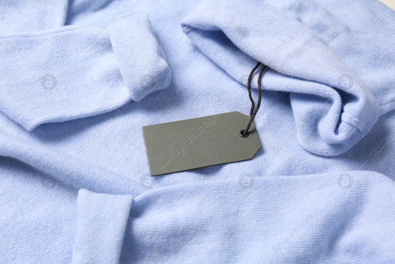 Photo of Blank grey tag on light blue sweater. Space for text