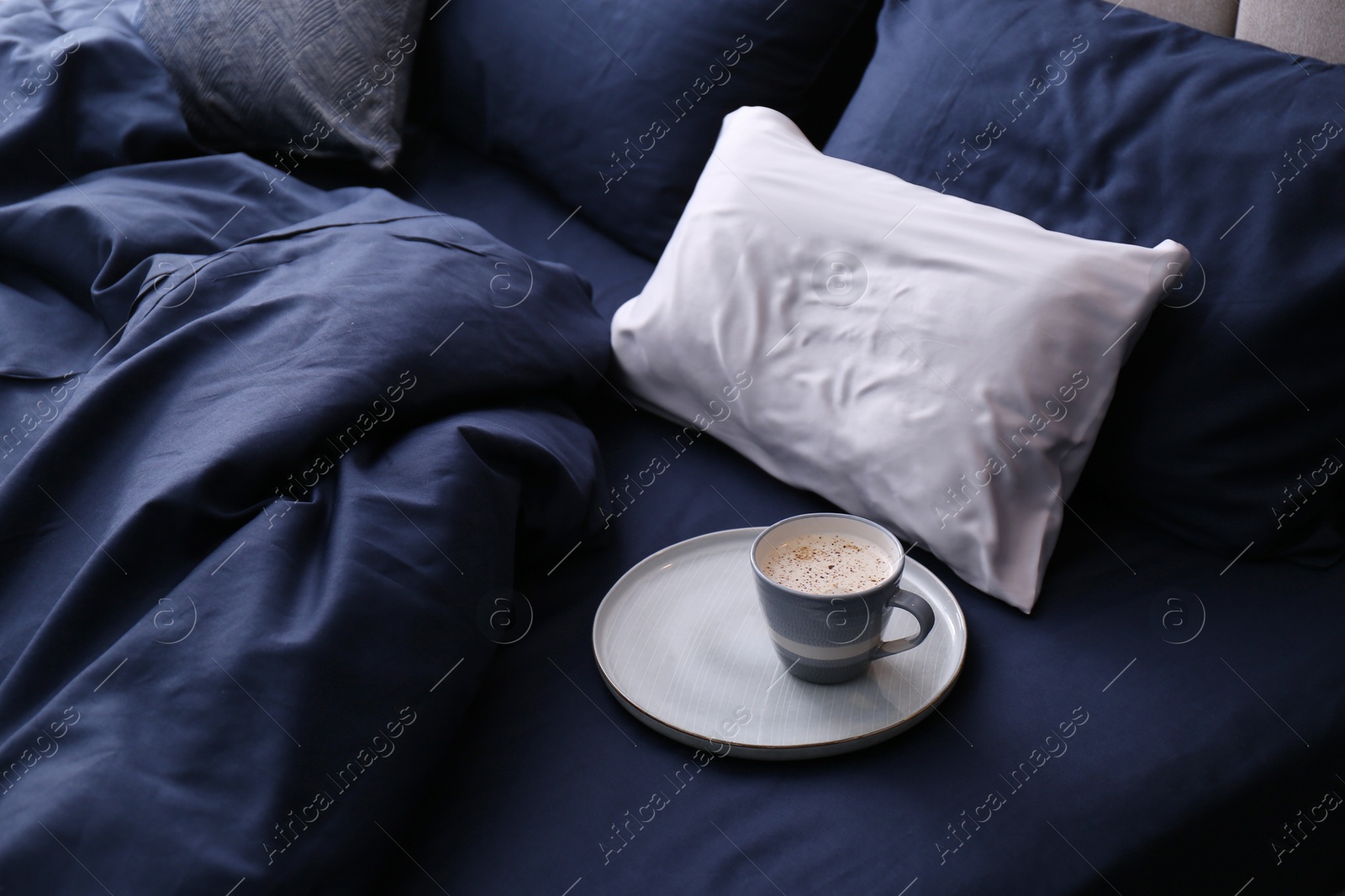 Photo of Cup of coffee on bed with stylish silky linens