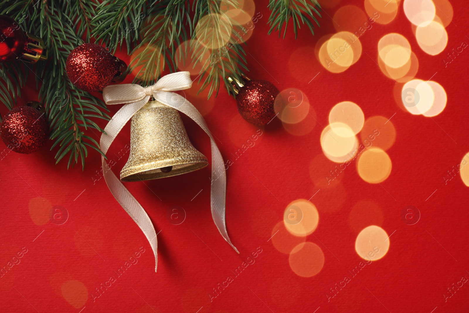 Photo of Christmas bell and fir tree branches with festive decor on red background, flat lay. Space for text