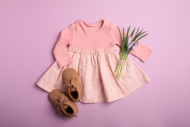 Photo of Flat lay composition with child's clothes, booties and flowers on pink background