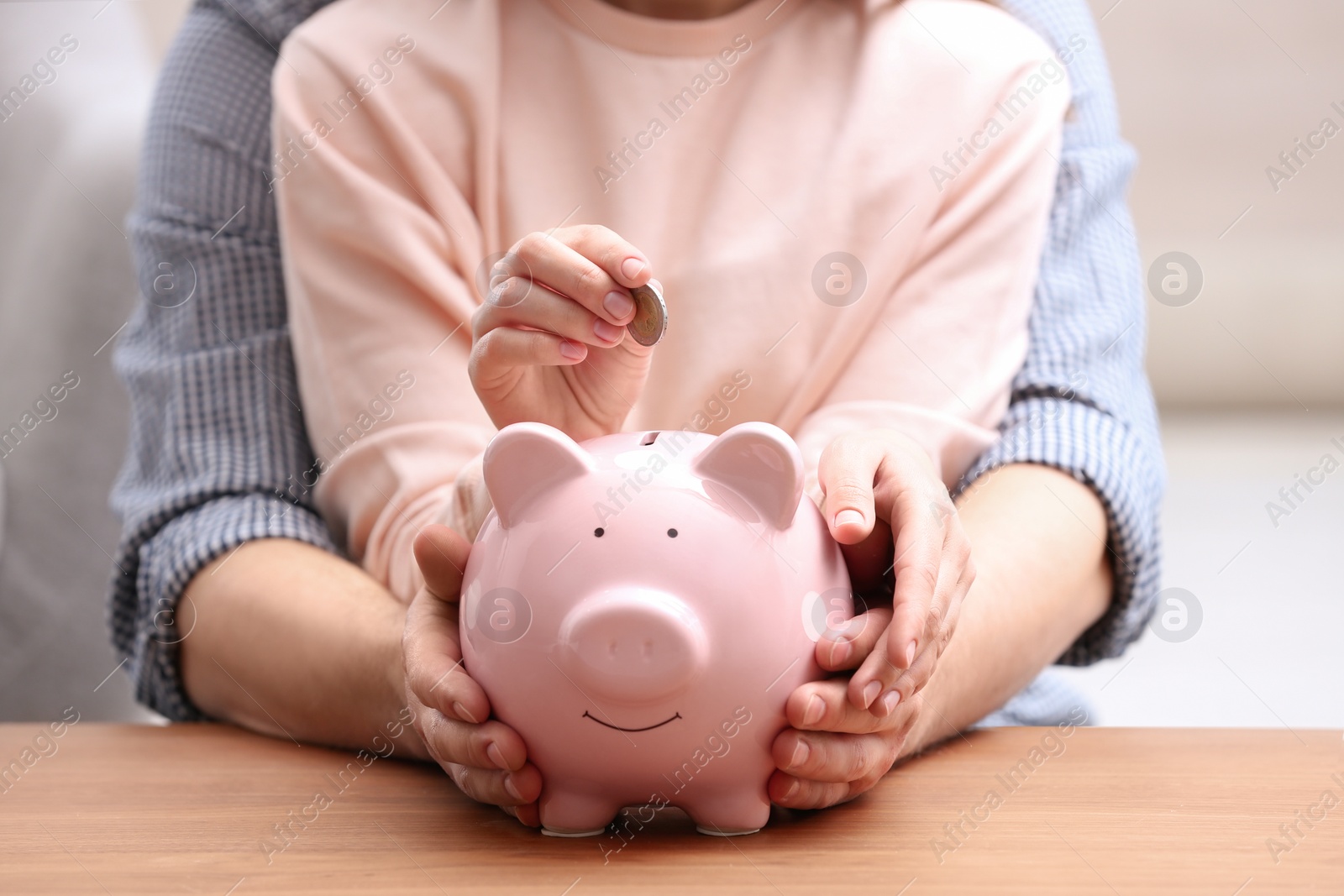 Photo of Couple with piggy bank and coin at wooden table, closeup