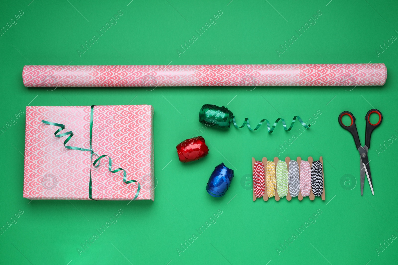 Photo of Flat lay composition with roll of wrapping paper, gift and accessories on green background