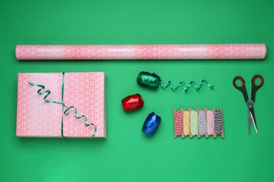 Photo of Flat lay composition with roll of wrapping paper, gift and accessories on green background