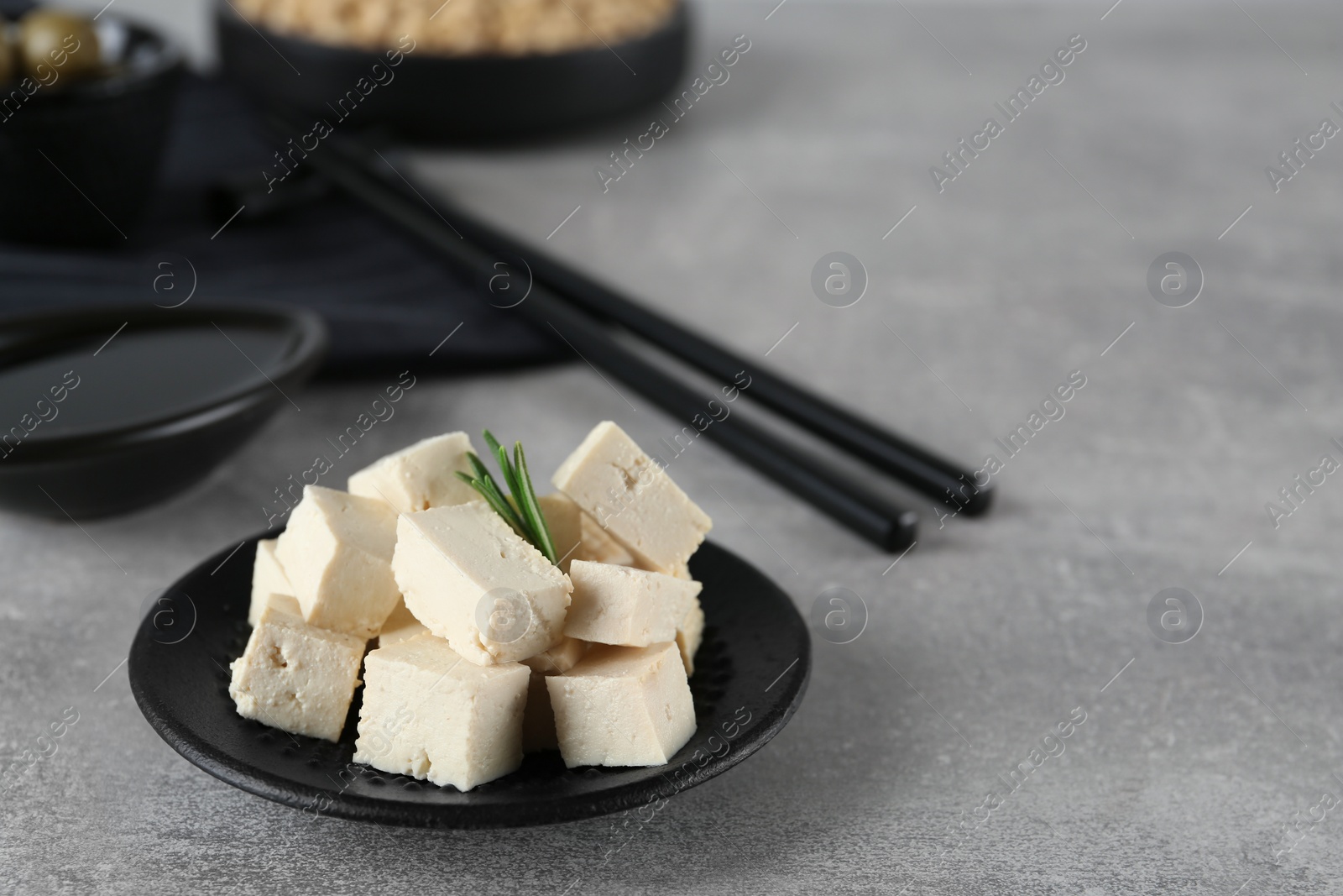 Photo of Pieces of delicious tofu with rosemary on grey table. Space for text