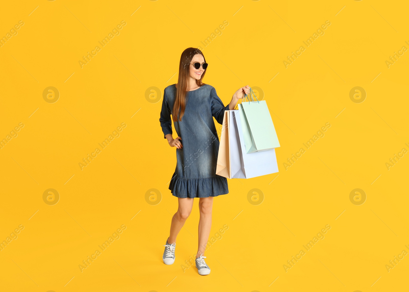 Photo of Beautiful young woman with paper shopping bags on yellow background