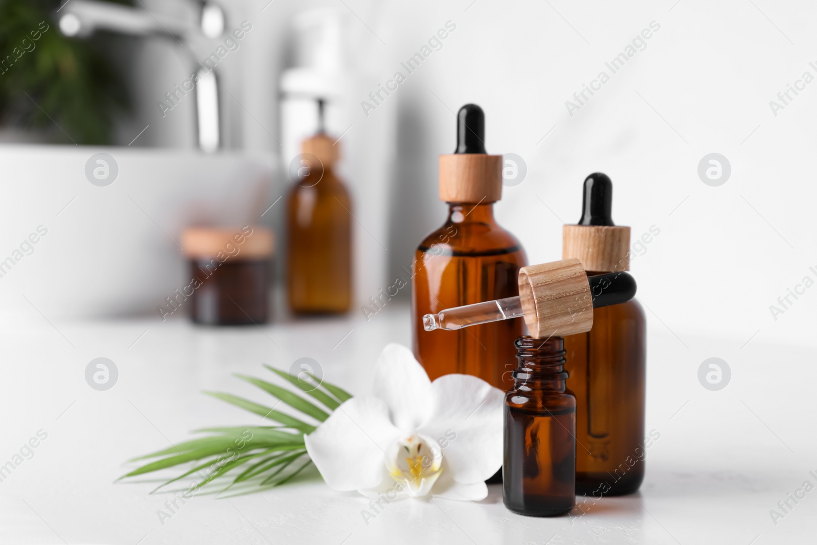 Photo of Essential oils and orchid flower on white table in bathroom, closeup