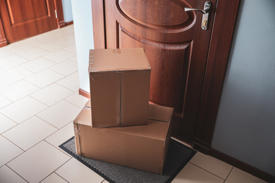 Photo of Cardboard boxes on rug near door. Parcel delivery service