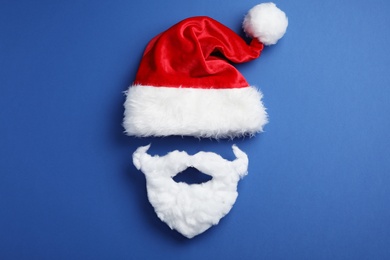 Santa Claus hat and beard on blue background, flat lay