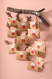 Photo of Gifts in envelopes with deer faces hanging on pink wall. Christmas advent calendar