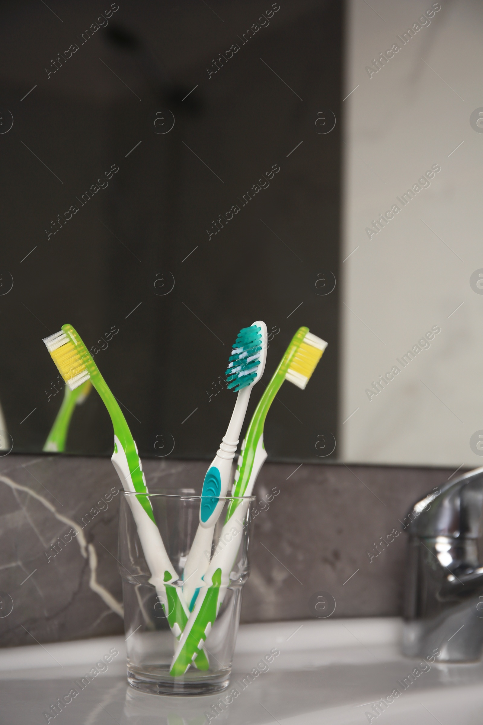 Photo of Light blue and green toothbrushes in glass holder on washbasin