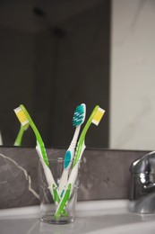 Photo of Light blue and green toothbrushes in glass holder on washbasin